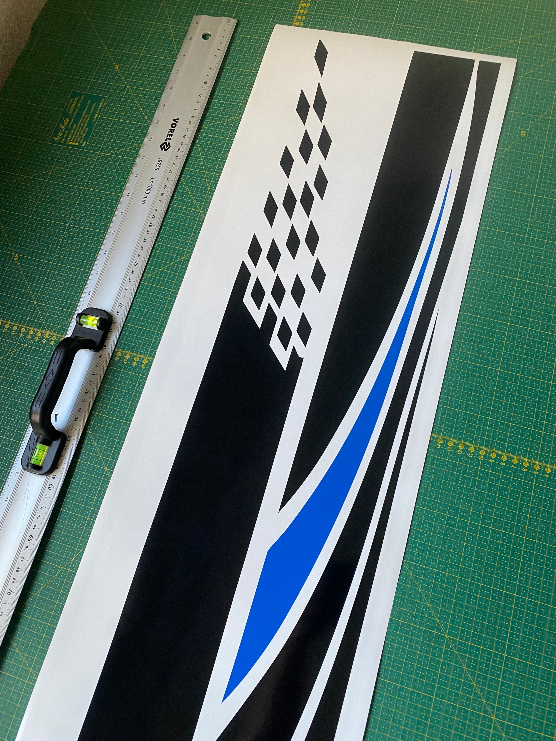 A vinyl decal sticker for Nissan Rogue with a 2 color design, laid out on a flat surface with a measuring tape for scale.