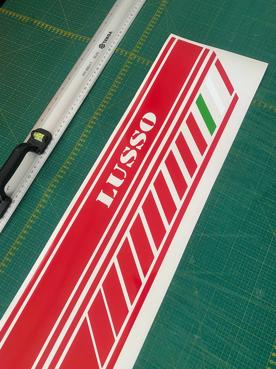 Red and white LUSSO logo decal on a green cutting mat with a ruler.