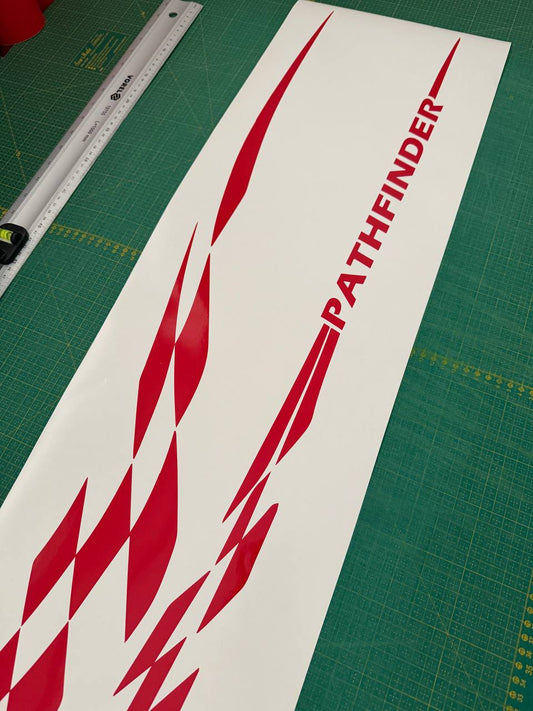 A long white vinyl decal sheet featuring red geometric chevron patterns and the word 'PATHFINDER' in red, laid diagonally on a green cutting mat with a ruler visible in the corner.