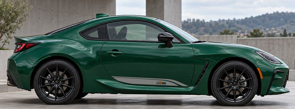 A dark green sports coupe car shown in a side profile view, parked outdoors near a concrete structure with hills in the background.
